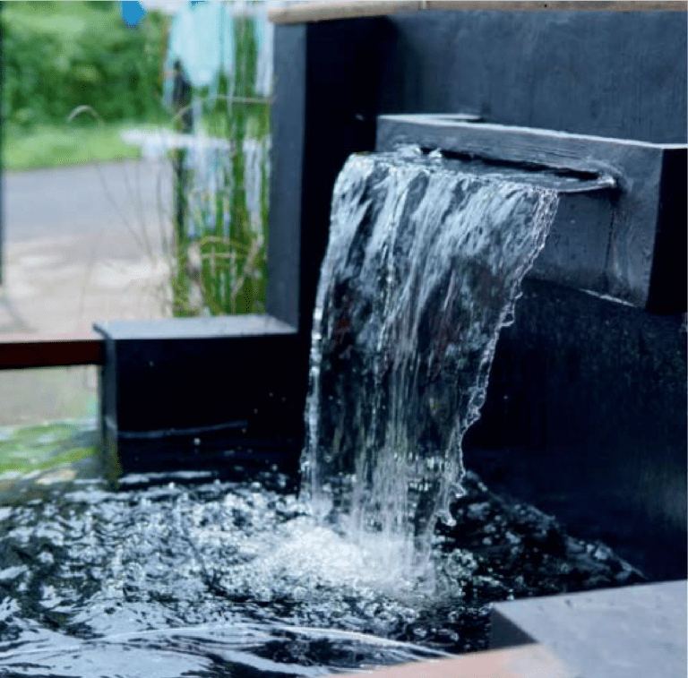 A small, modern outdoor waterfall feature with clear water cascading into a pool.