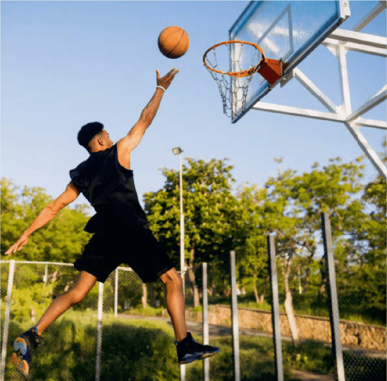 Man jumping to shoot a basketball at an outdoor court.